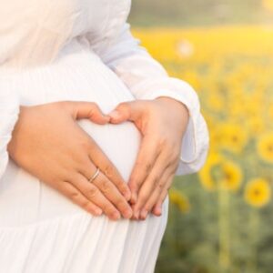 Zwangerschap, jonge vrouw, zwangere buik, natuur, zonnebloemveld, handen met buik